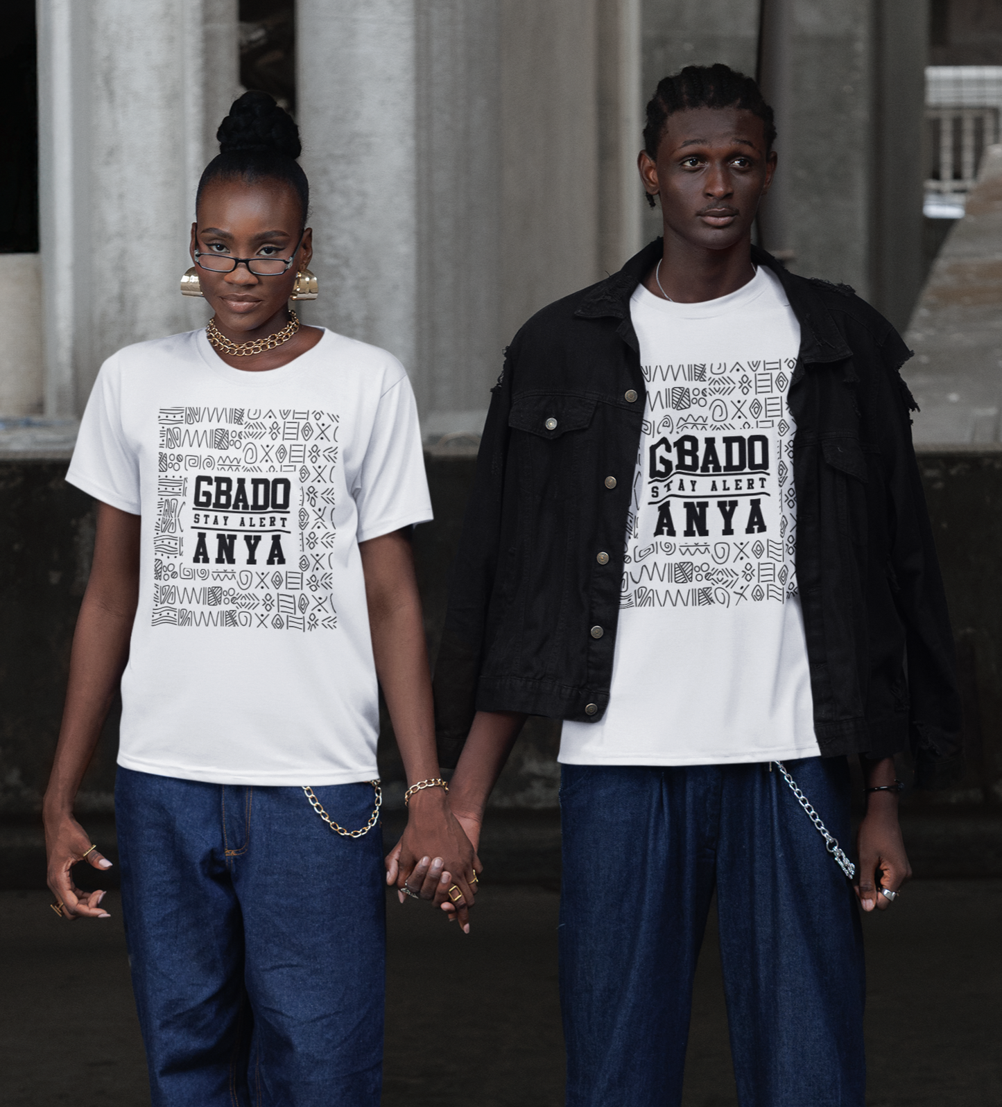 Two people wearing matching white t-shirts with text, standing in front of classical architecture.