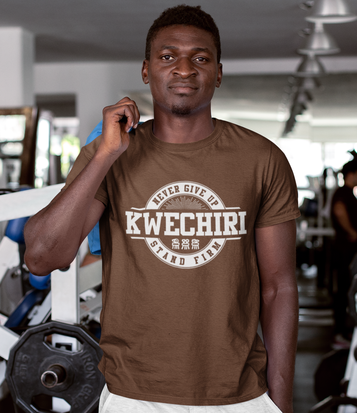 Man wearing a brown t-shirt with 'Kwechiri' branding in a gym setting