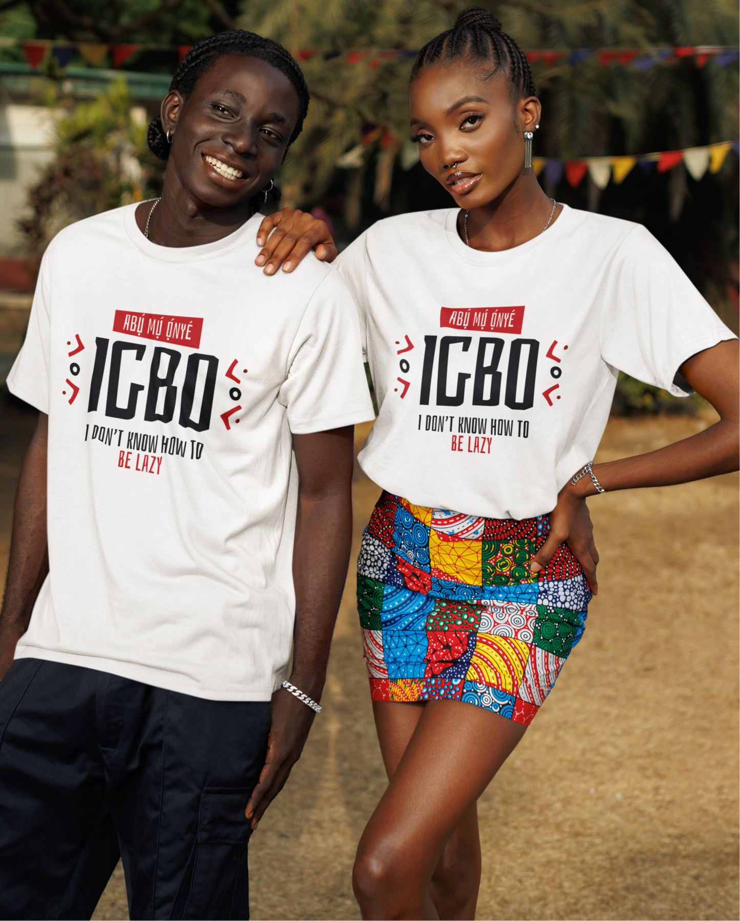 Two people wearing white t-shirts with 'IGBO' text, standing outdoors with greenery in the background.
